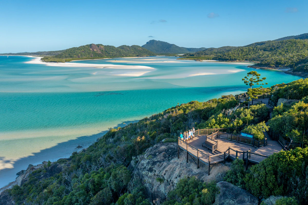 White sand swirling through turquoise water below a wooded lookout